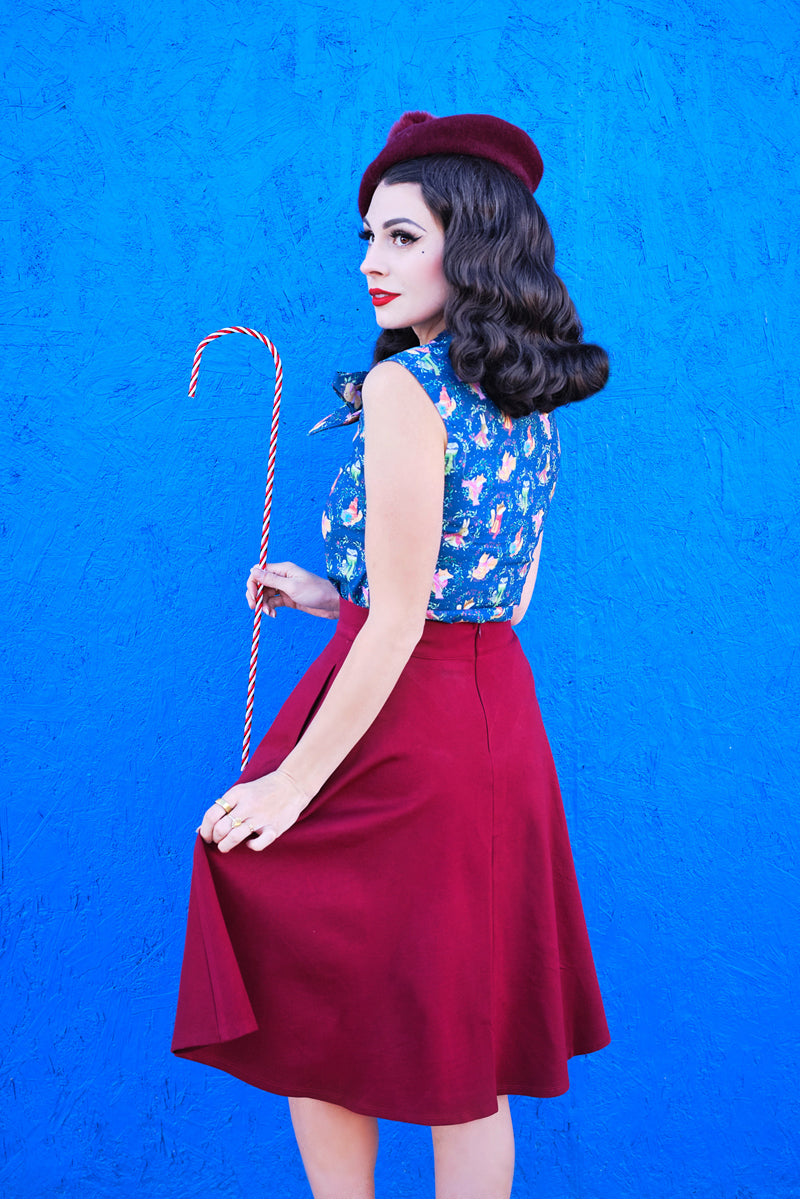 a model standing in front of a brigth blue wall wearing the charlotte skirt in burgundy