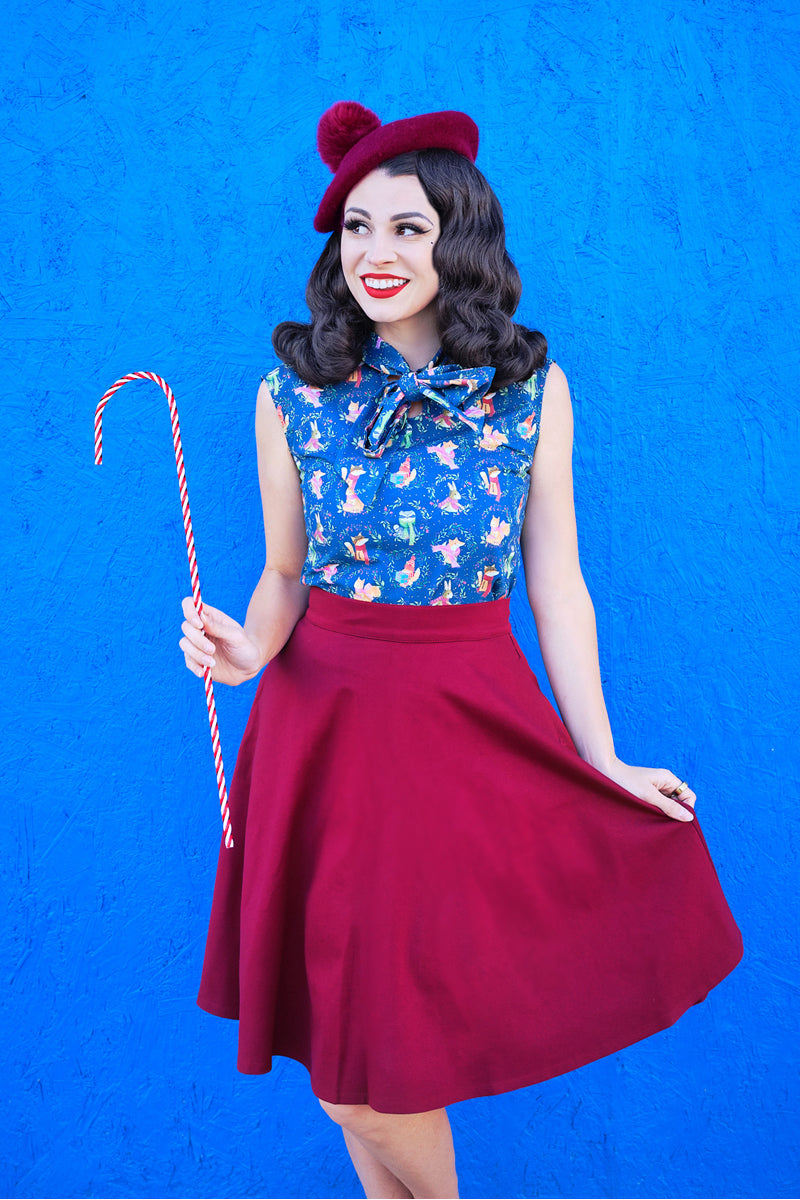 a model standing in front of a brigth blue wall wearing the charlotte skirt in burgundy