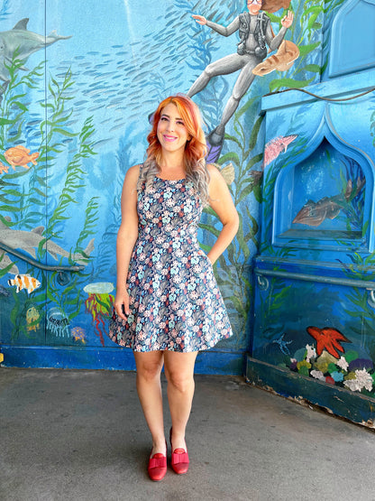 a model standing in front of an ocean life mural wearing the coral skater dress
