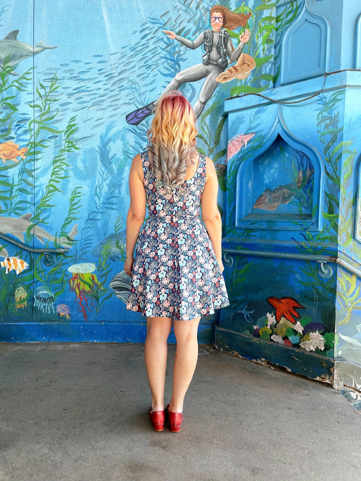 a back view of model standing in front of an ocean life mural wearing the coral skater dress