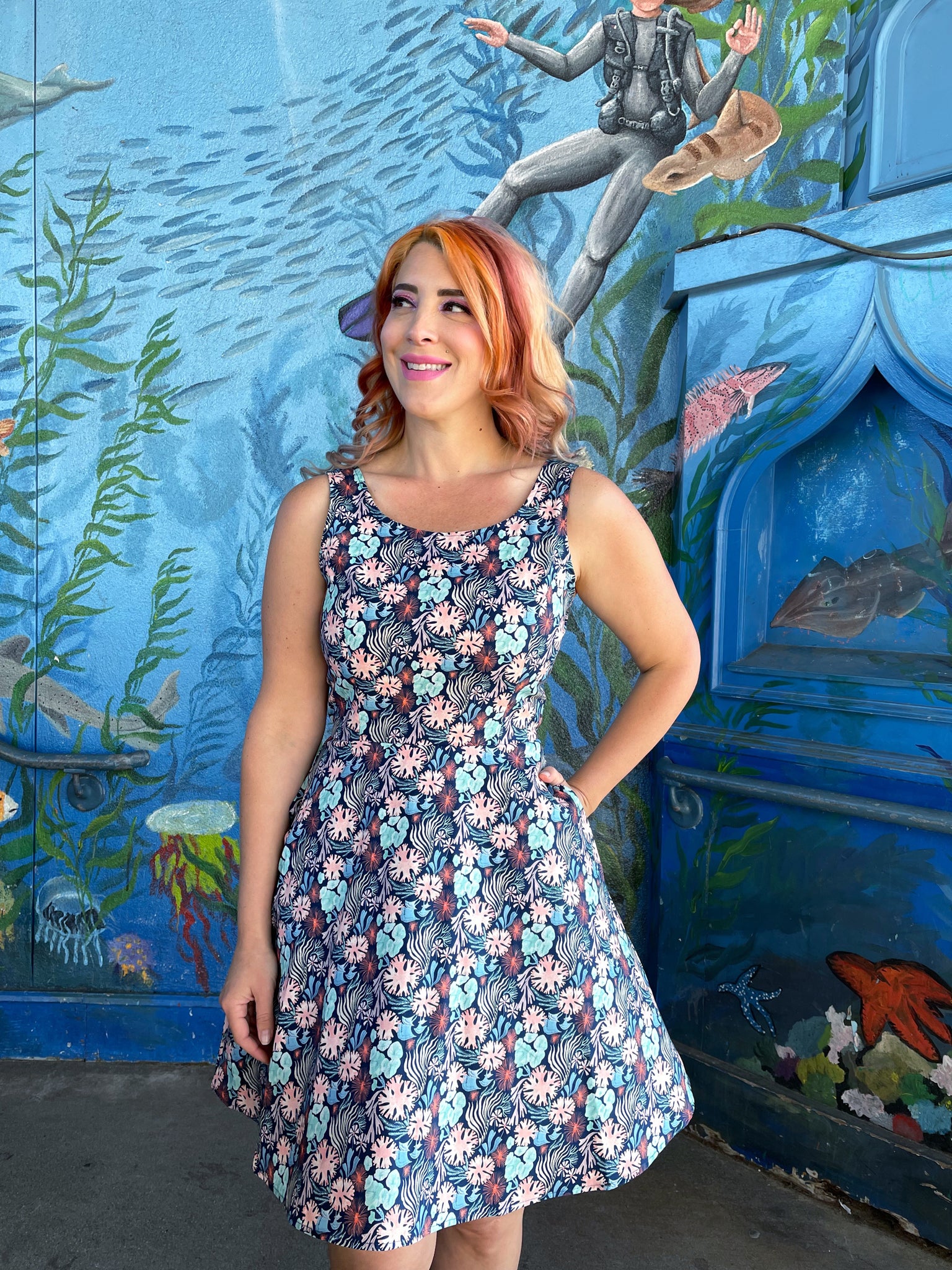 a model standing in front of an ocean life mural wearing the coral skater dress