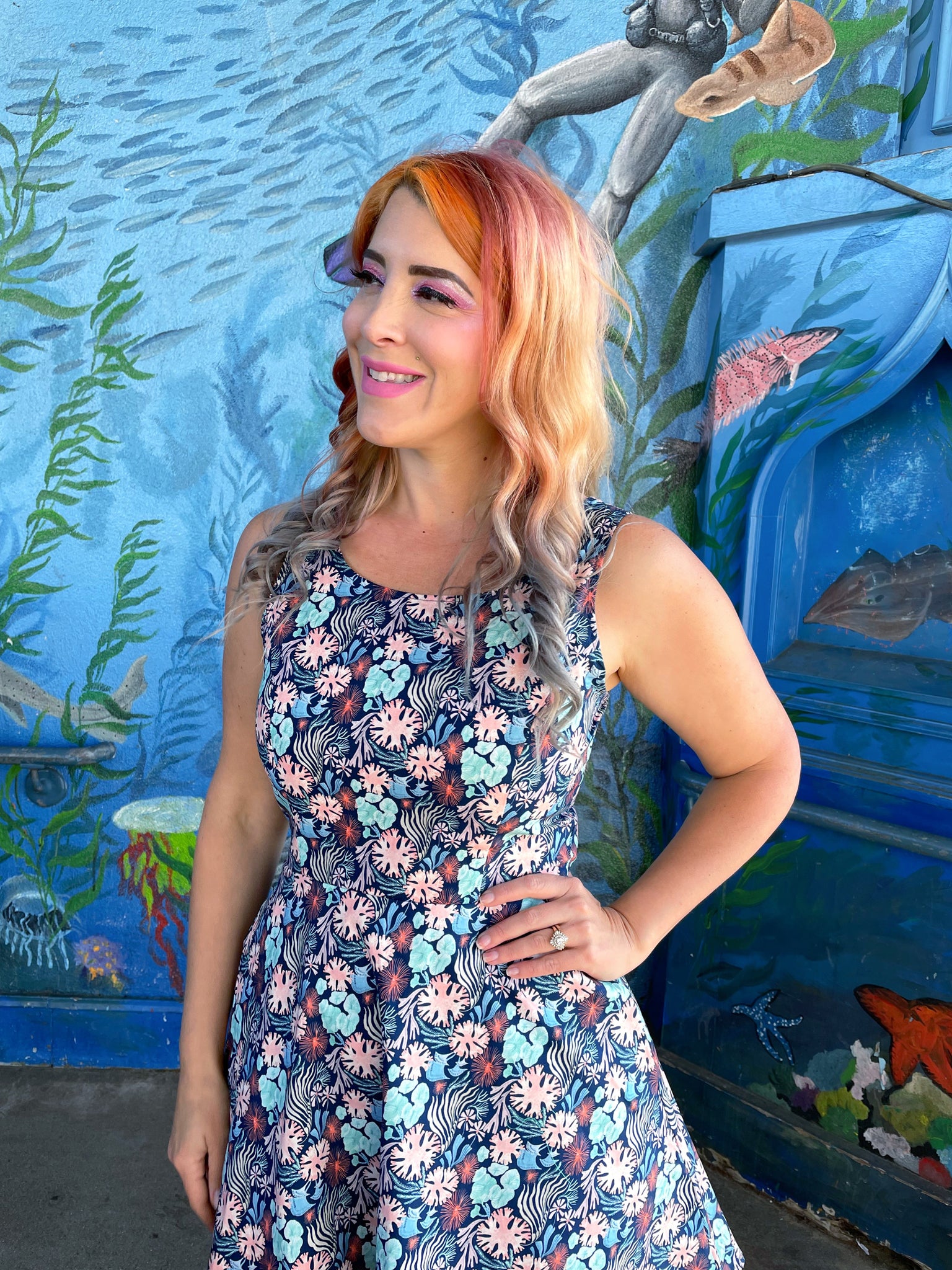a close up of model standing in front of an ocean life mural wearing the coral skater dress