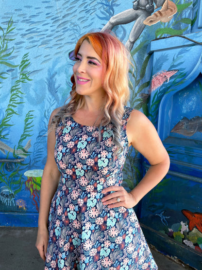 a close up of model standing in front of an ocean life mural wearing the coral skater dress