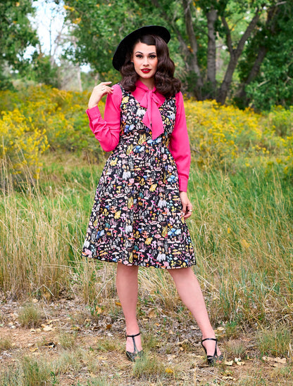 a full length of a model standing in front of trees wearing the helen retro blouse in pink underneath a dress