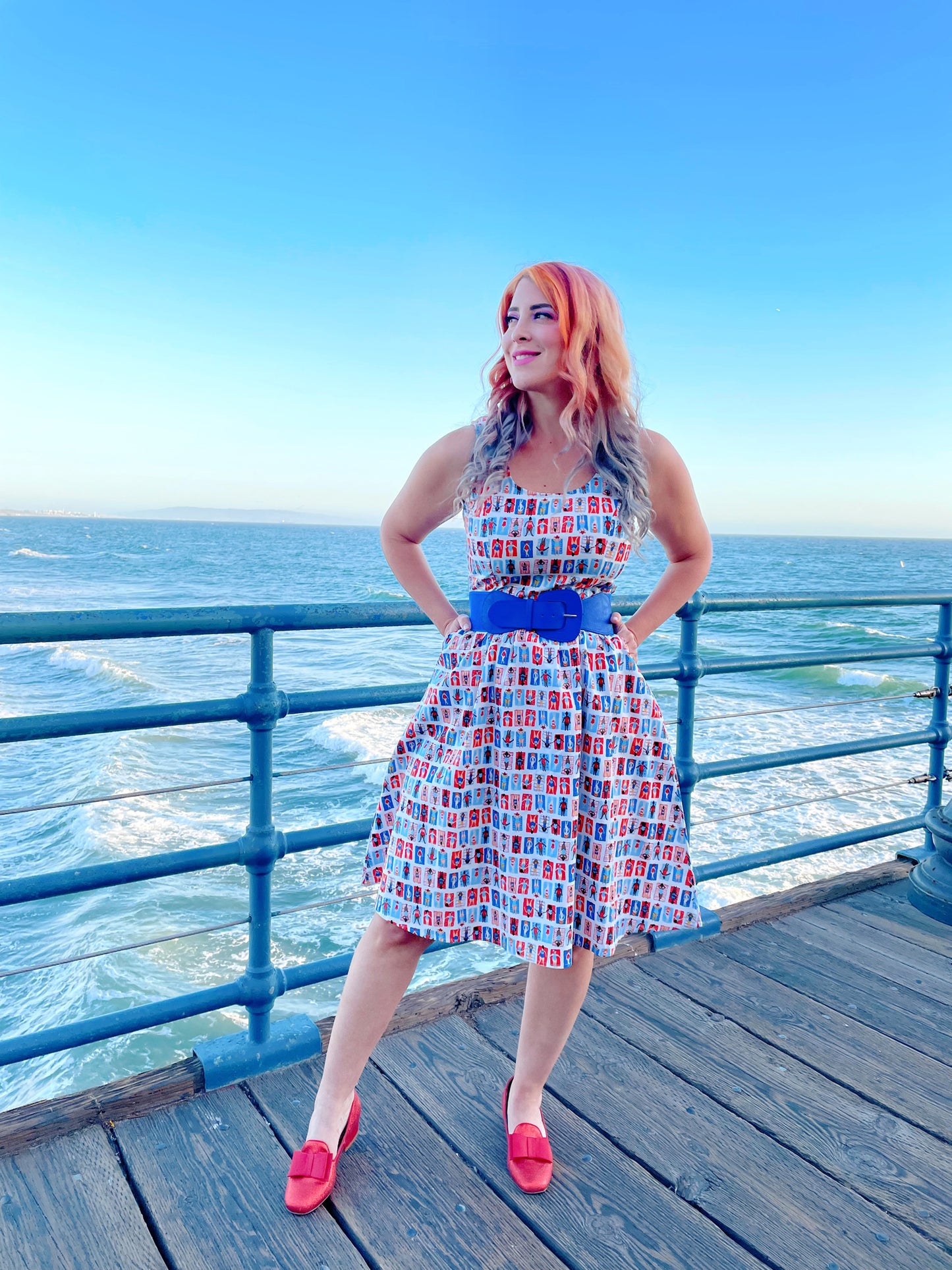 a model standing on a boardwalk with the ocean in the backgroun wearing the sunny days fit and flare dress