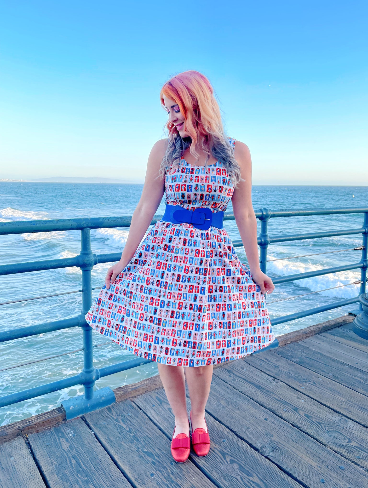 a model standing on a boardwalk with the ocean in the backgroun wearing the sunny days fit and flare dress
