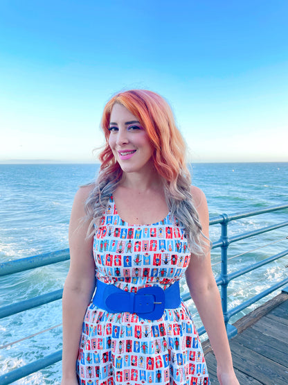 a close up of model standing on a boardwalk with the ocean in the backgroun wearing the sunny days fit and flare dress
