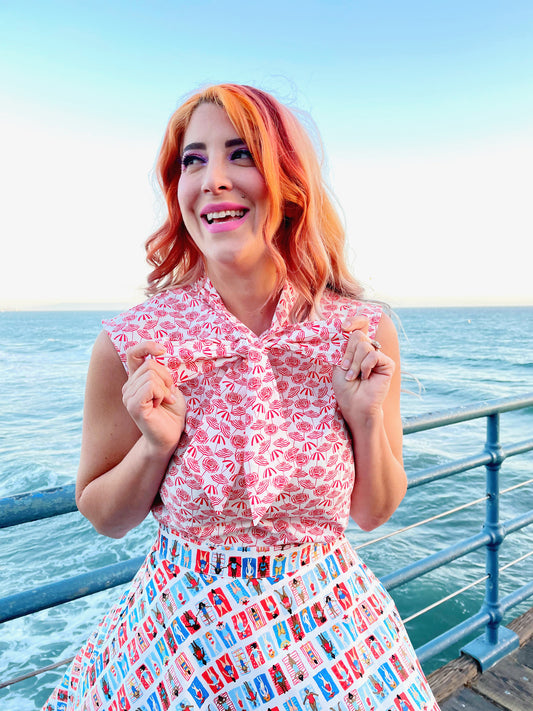 a close up of a model standing in front of the ocean wearing our sleeveless bow tie blouse with umbrella fabric