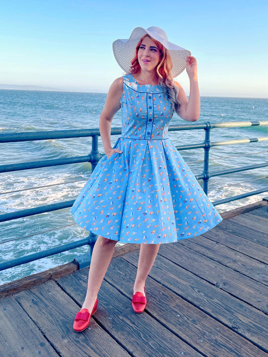 a model standing on the boardwalk in front of the ocean wearing elizabeth dress in windsurfer and white sun hat