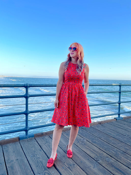 a model standing on the boardwalk in front of the ocean wearing sunglasses vintage dress and red sunglasses