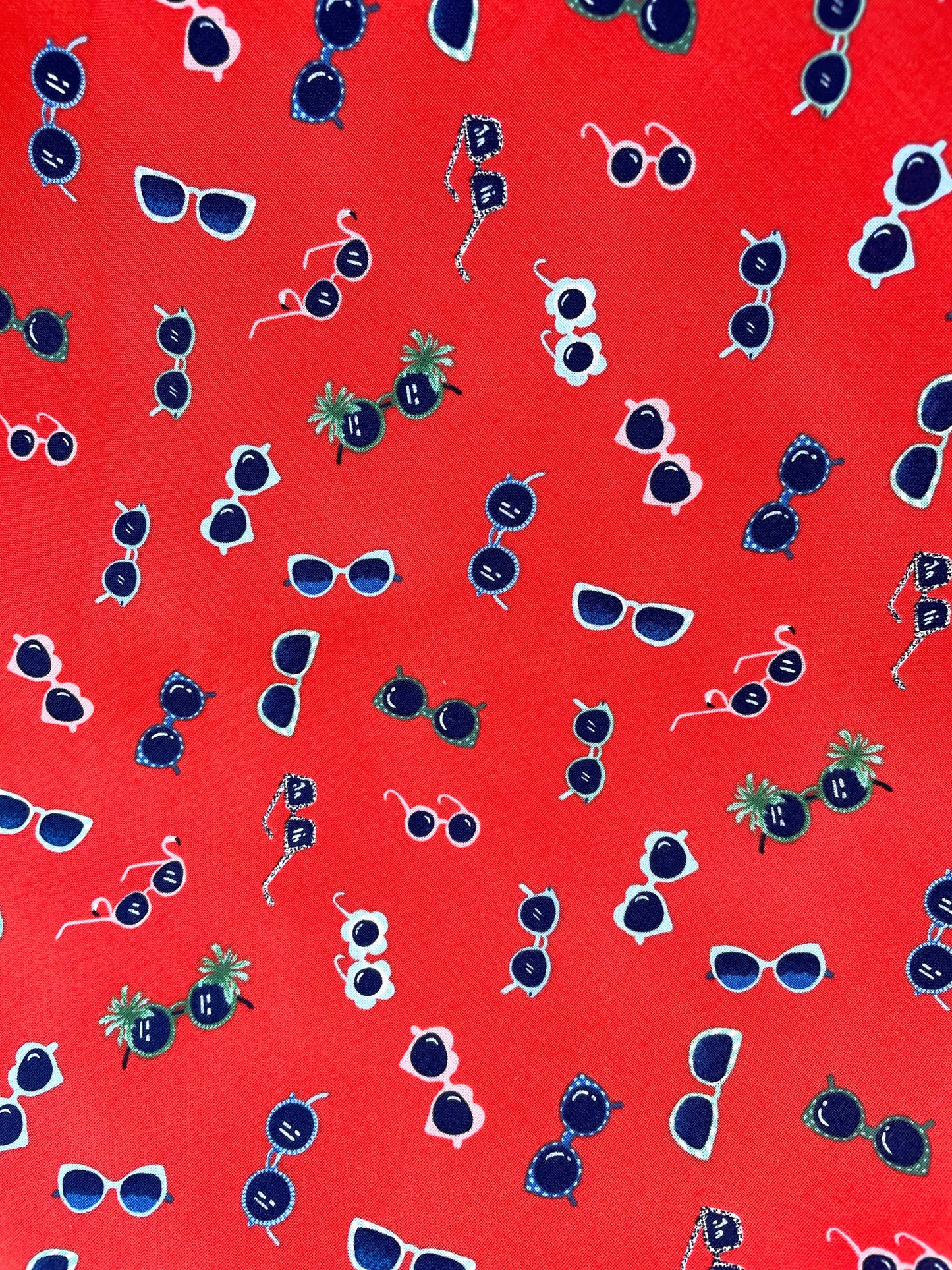 a close up of fabric showing tossed sunglasses print on red background