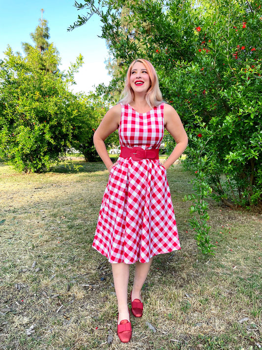 a model standing outdoors wearing gingham midi dress wtih red belt