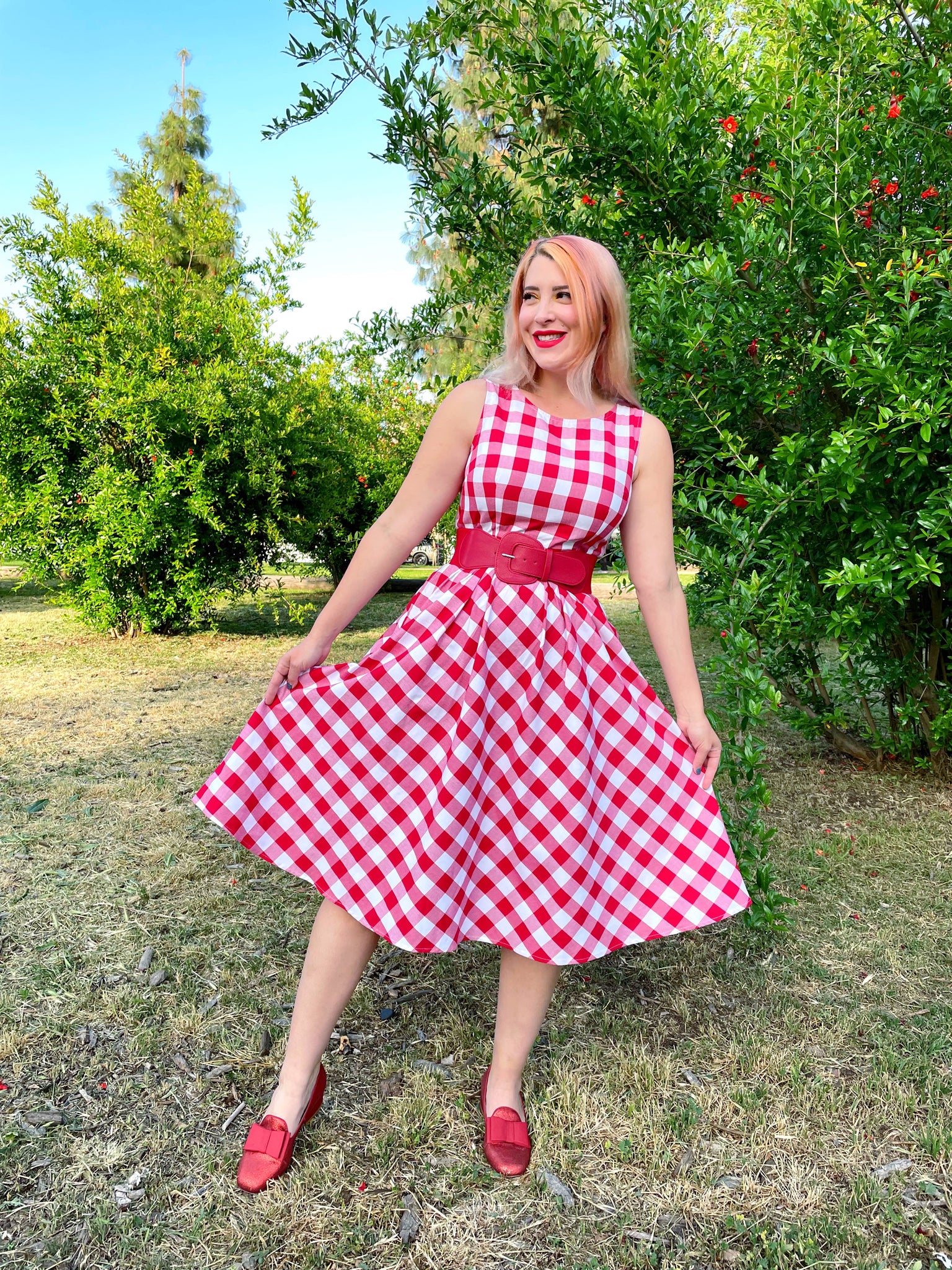 a model standing outdoors wearing gingham midi dress wtih red belt