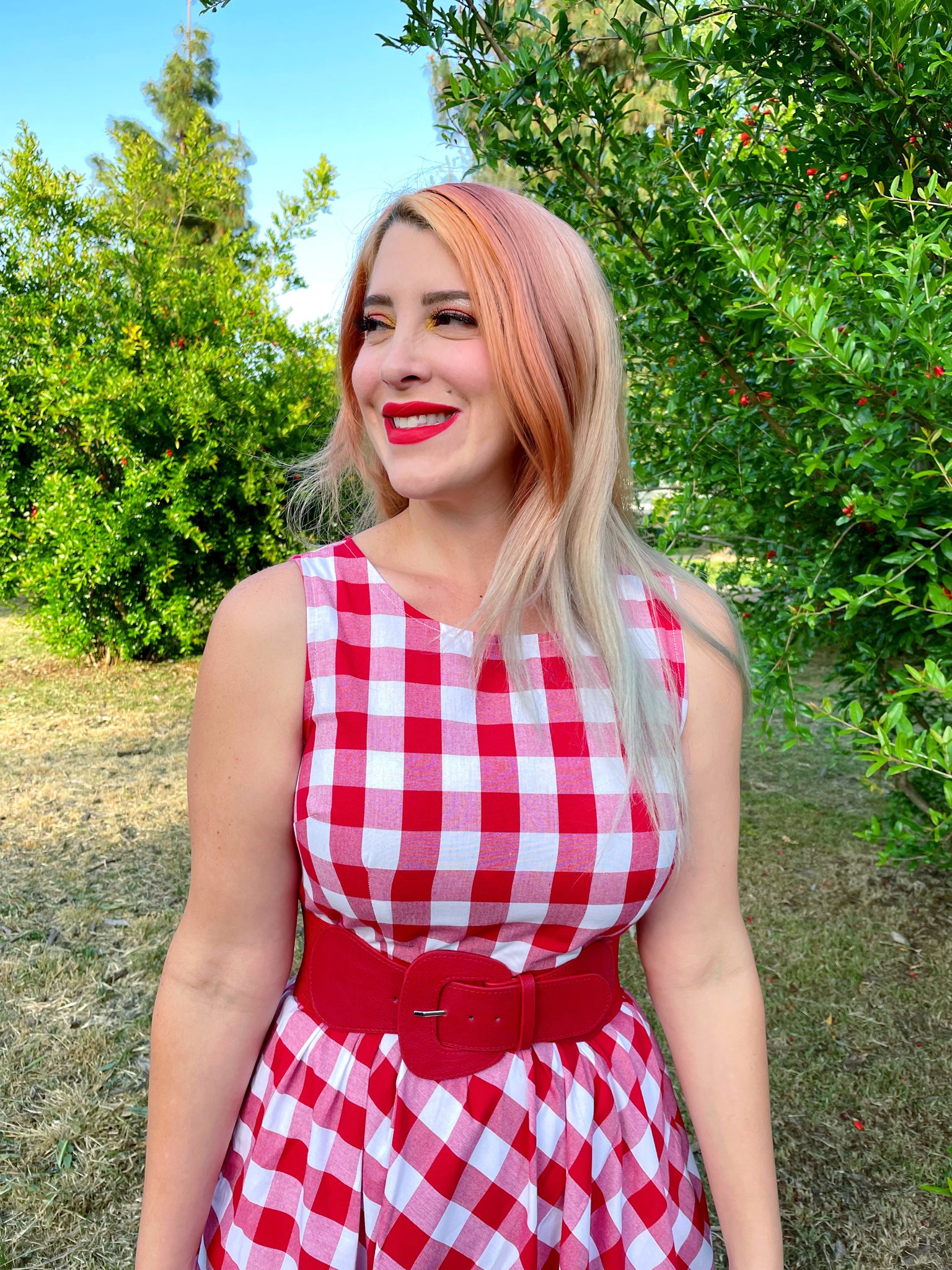 a close up of model standing outdoors wearing gingham midi dress wtih red belt