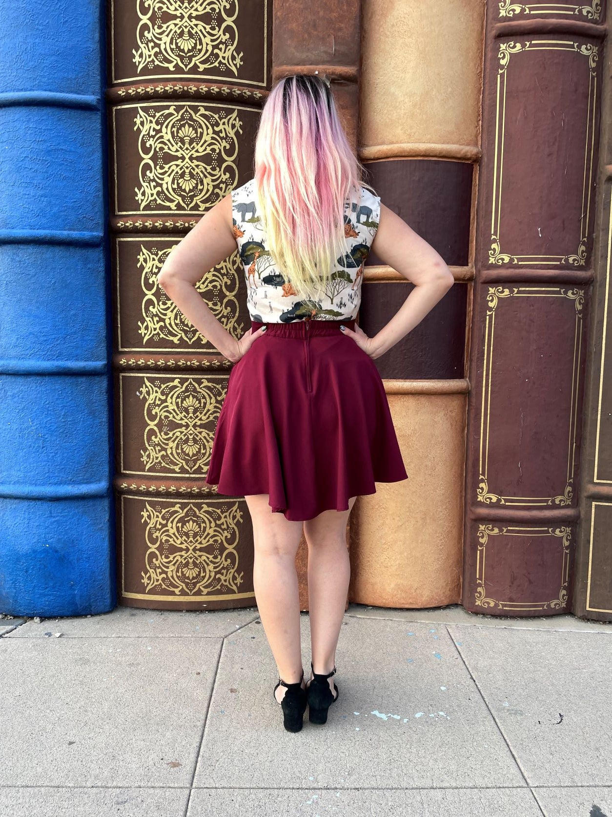 a full image of a back of a model standing in front of large book decorations wearing the burgundy skater skirt
