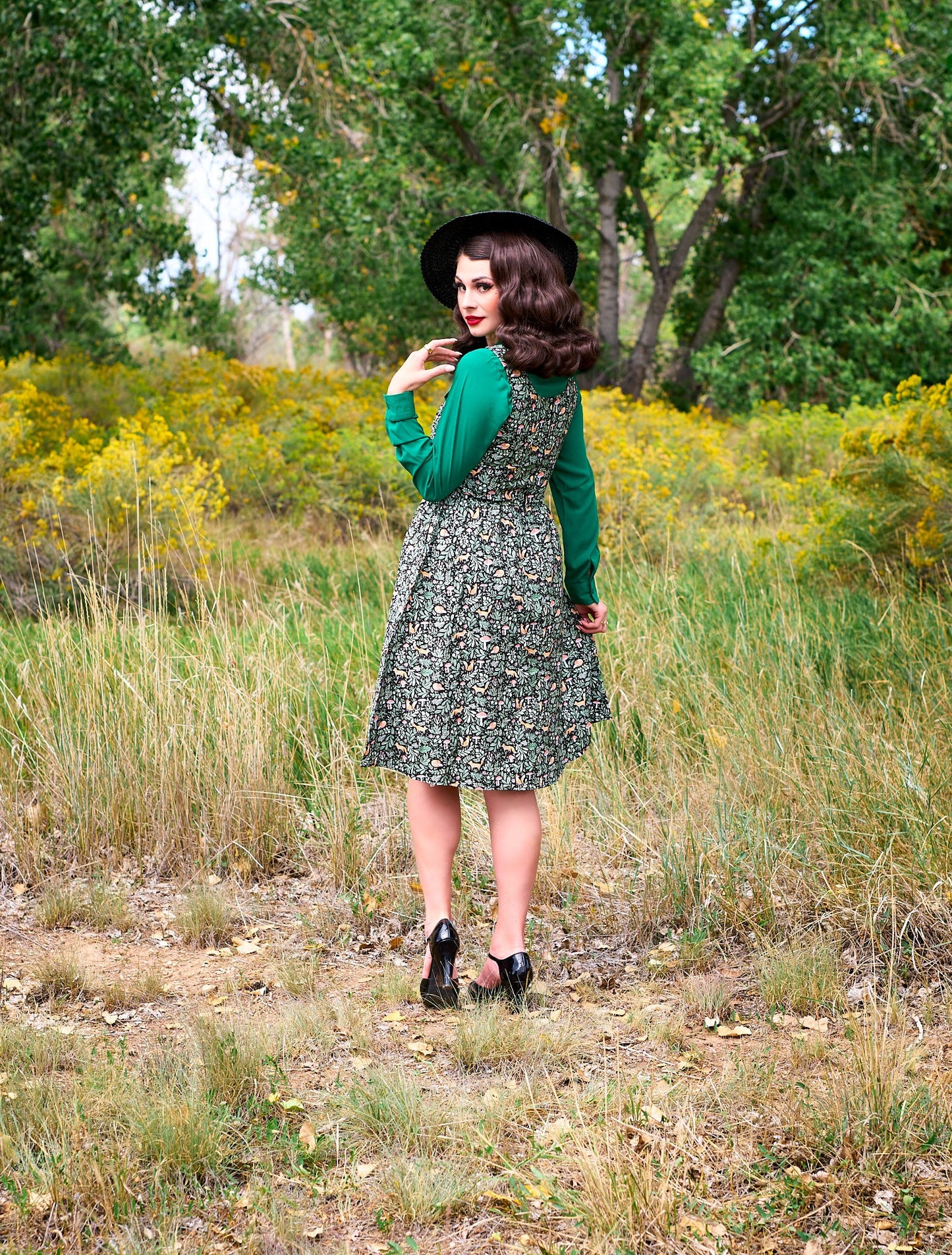 a full size image of the back side of a model standing outdoors in front of trees wearing the foxy fit and flare dress