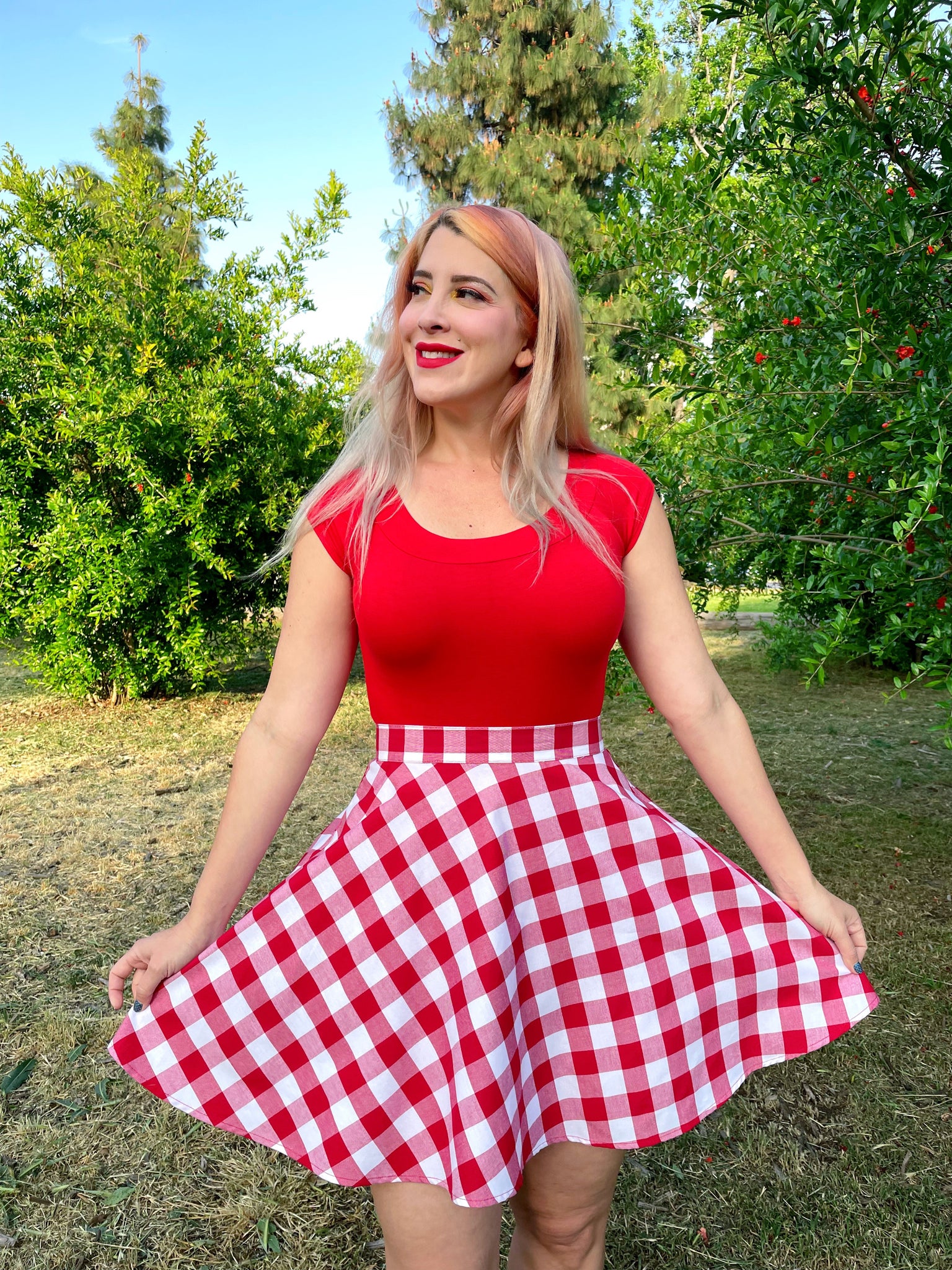 a close up of a model outdoors in front of trees wearing red gingham skater skirt