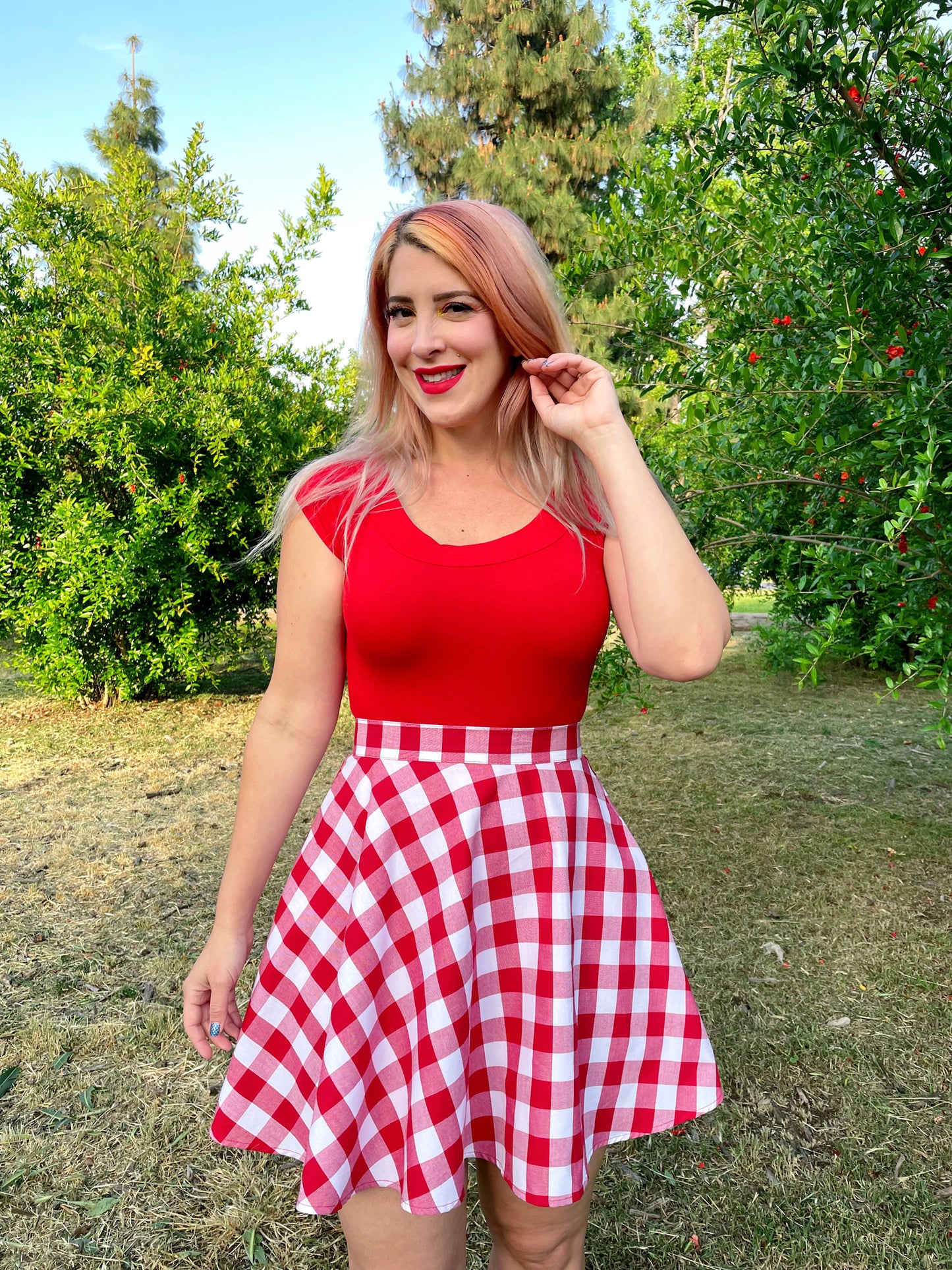 a close up of a model outdoors in front of trees wearing red gingham skater skirt