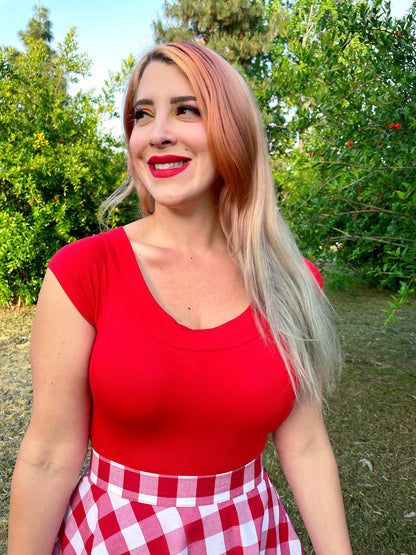 a close up of a model standing in front of trees wearing our boat neck top in red
