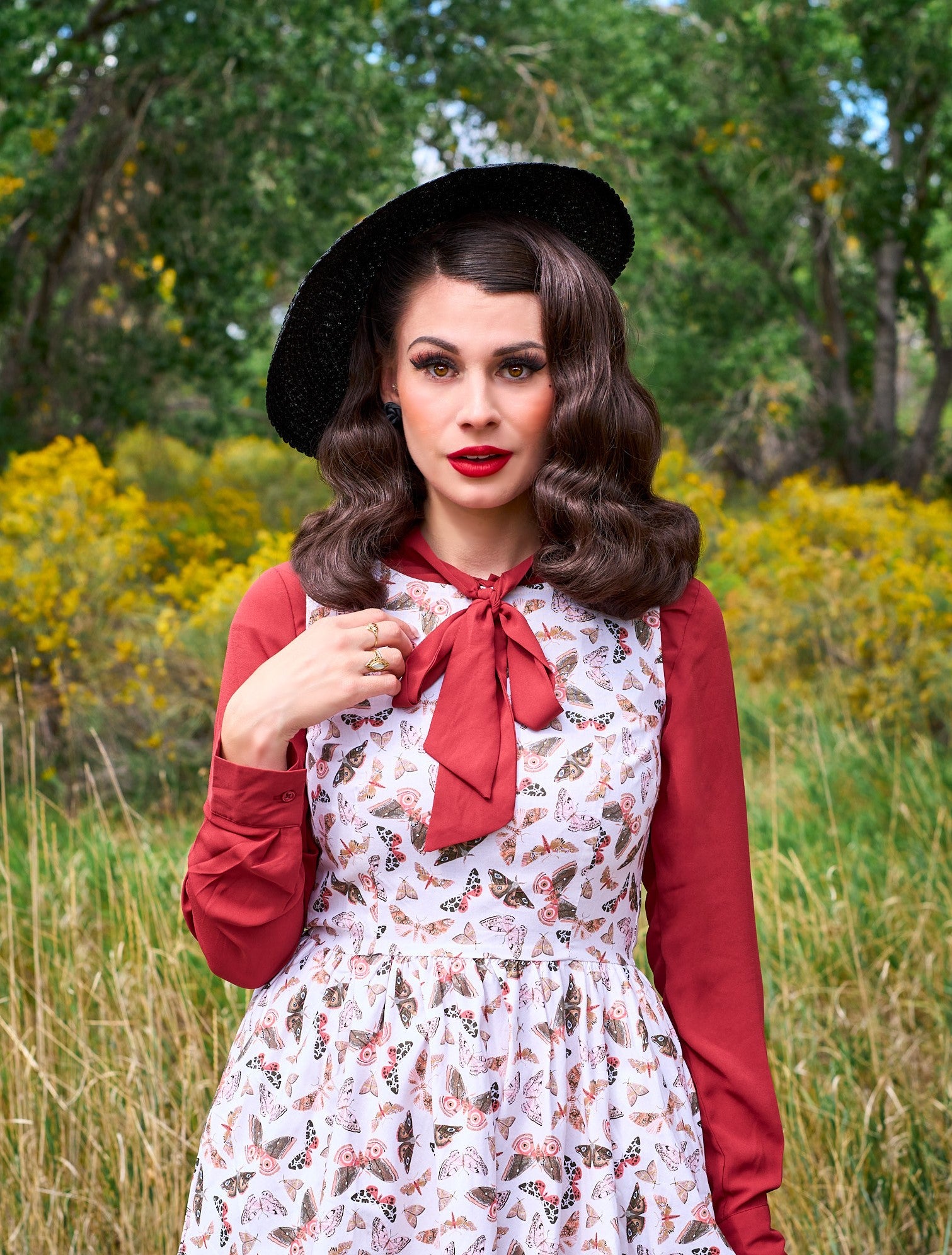 a close up of a model standing in front of trees wearing the helen retro blouse in cognac shown under a dress
