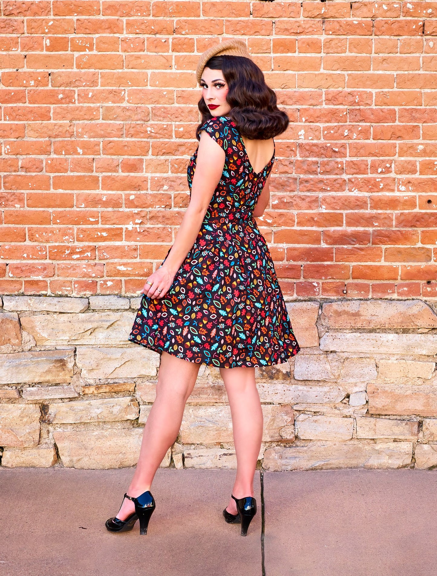 a back view of model standing in front of brick wall wearing the leaves and acorn margaret dress and beret