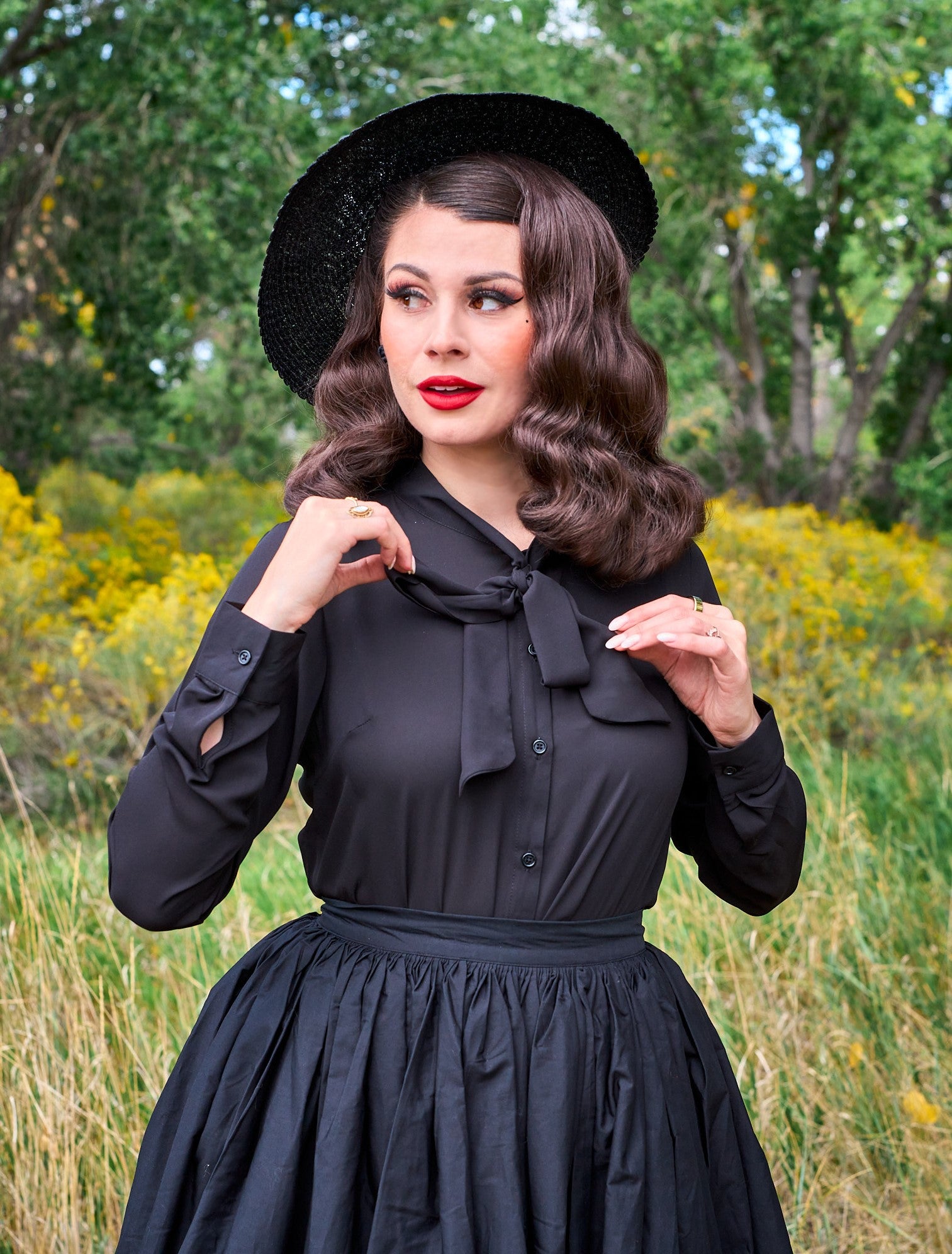 a close up of a model standing in front of trees wearing the helen retro blouse in black
