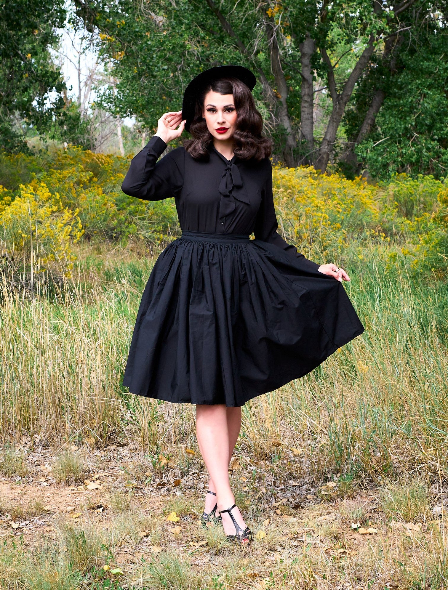 a full length of a model standing in front of trees wearing the helen retro blouse in black