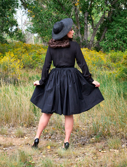 a full length of the back view of a model standing in front of trees wearing the helen retro blouse in black