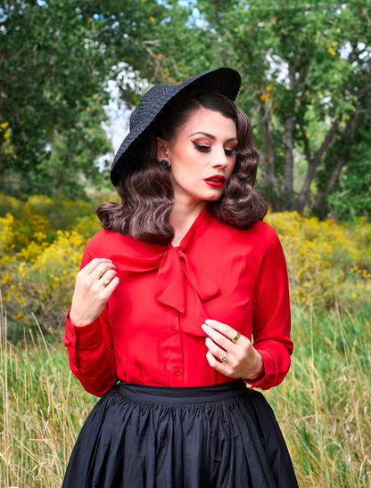 a close up of a model standing in front of trees wearing the helen retro blouse in red