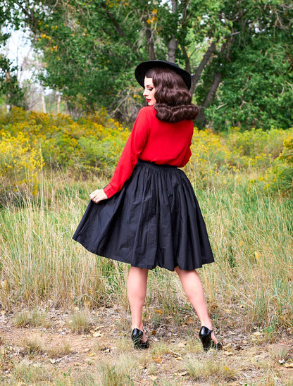 a full length of the back view of a model standing in front of trees wearing the helen retro blouse in red