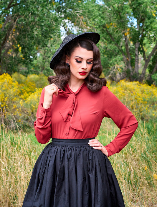 a close up of a model standing in front of trees wearing the helen retro blouse in cognac
