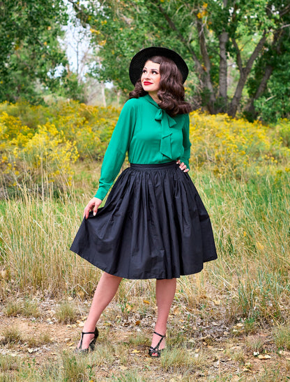 a full length image of a model standing in front of trees wearing the helen retro blouse in green