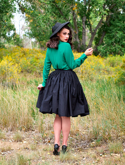 a full length of the back view of a model standing in front of trees wearing the helen retro blouse in green