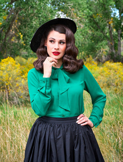 a close up of a model standing in front of trees wearing the helen retro blouse in green