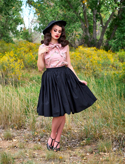 a full image of a model wearing our moth bow top and peggy skirt. she is holding one side of the skirt and looking down