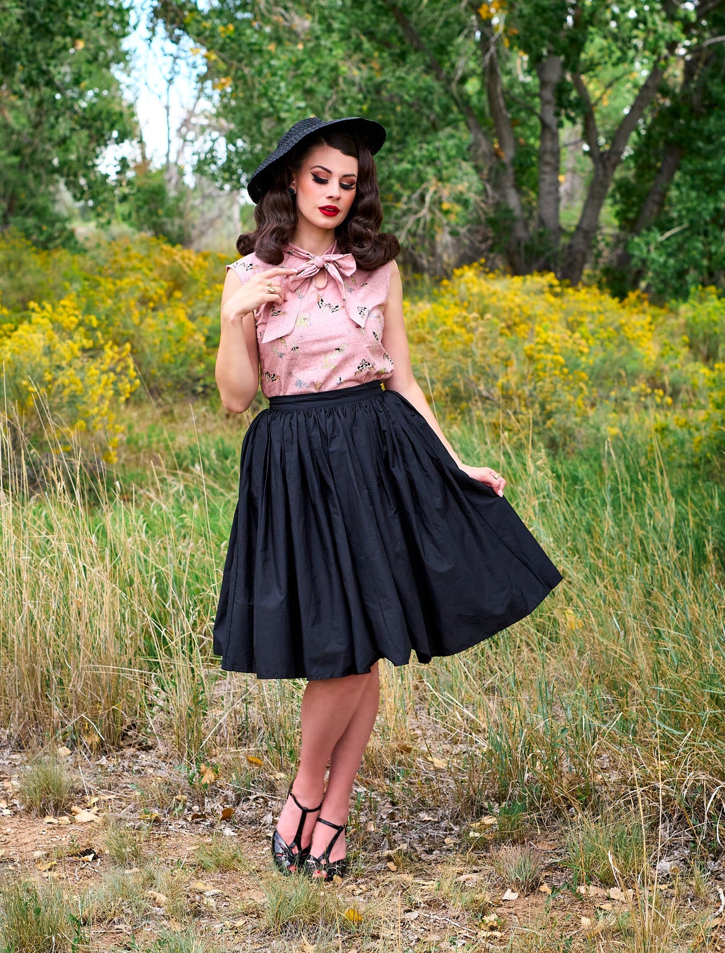 a full size image of a model standing outdoors in front of trees wearing the peggy swing skirt in black