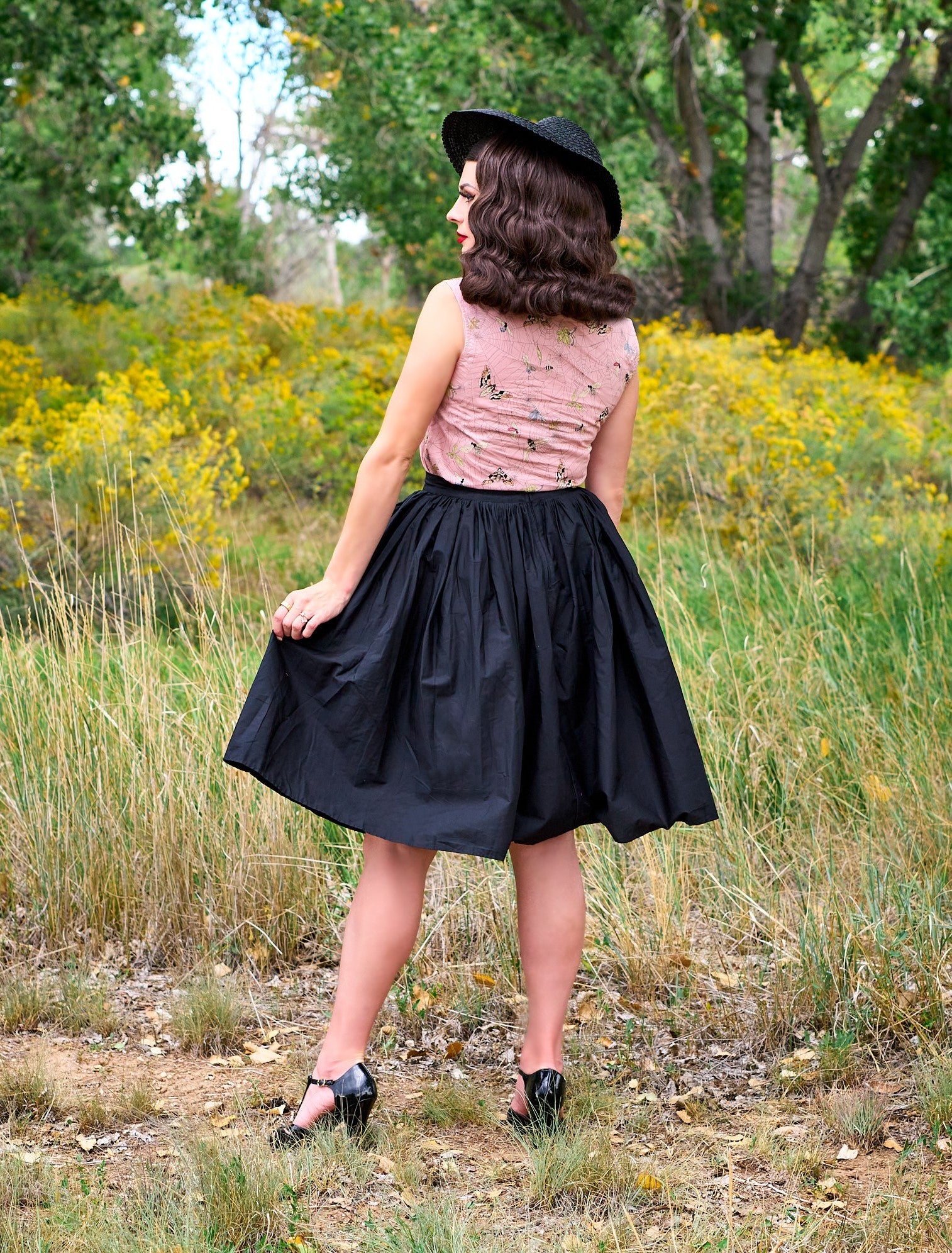 a full size image of the back side of a model standing outdoors in front of trees wearing the peggy swing skirt in black