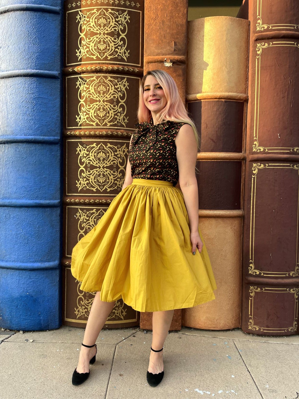 a full image of a model standing in front of books wearing peggy swing skirt in mustard