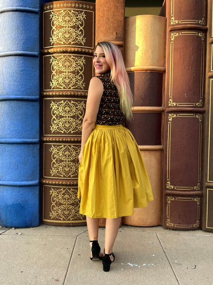a full image of a back of a model standing in front of books wearing peggy swing skirt in mustard