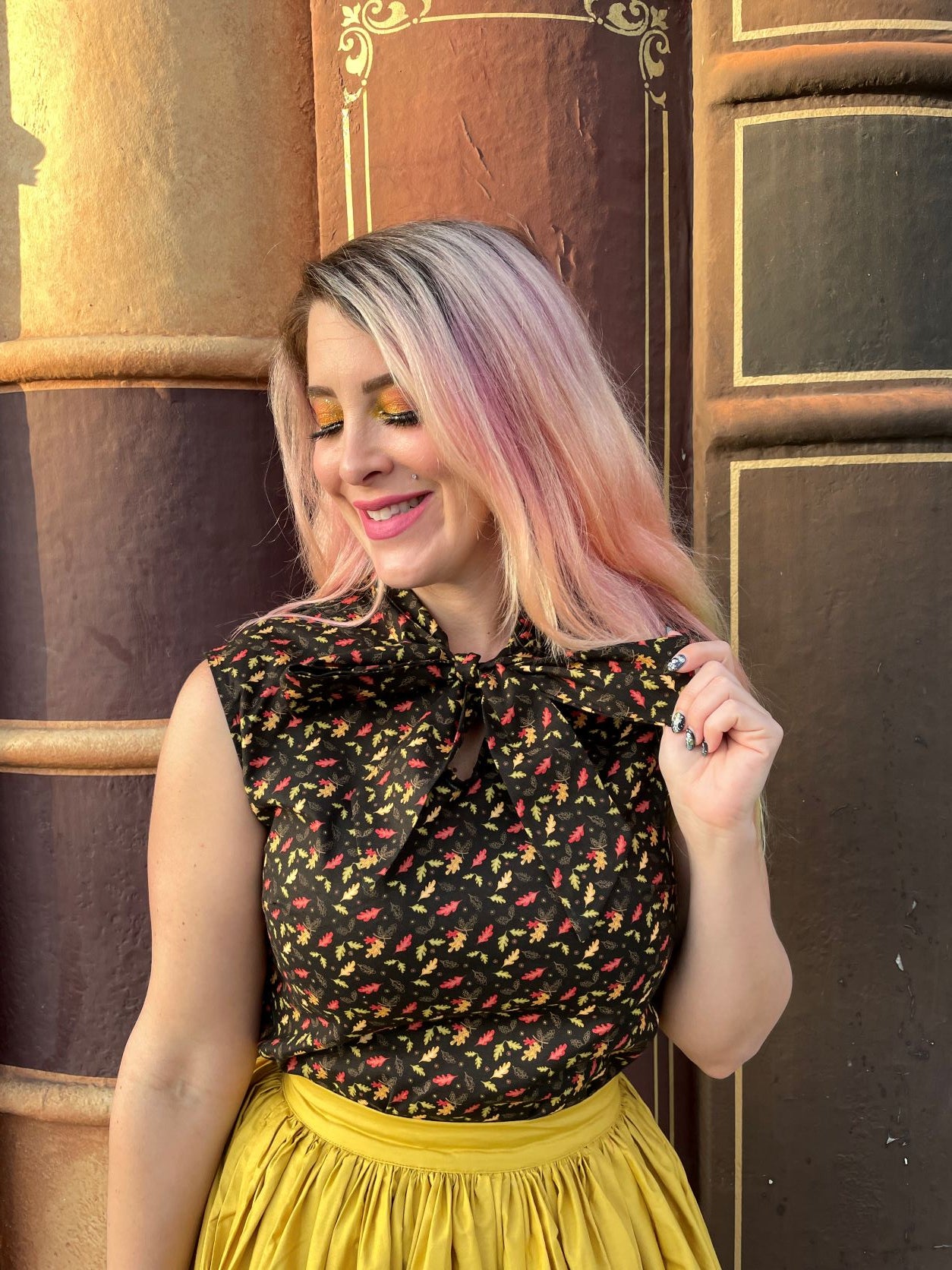 a close up of a model standing in front of books wearing leaves bow top and holding the ties of the bow