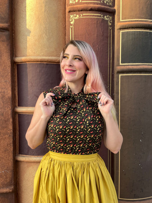 a close up of a model standing in front of books wearing leaves bow top and holding the ties of the bow