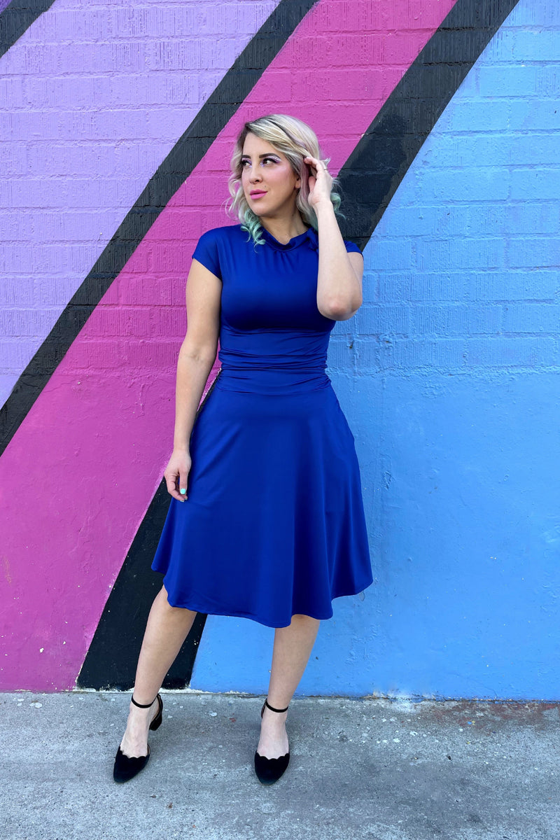 a full length of a model standing in front of a colorful wall wearing bombshell dress in royal blue