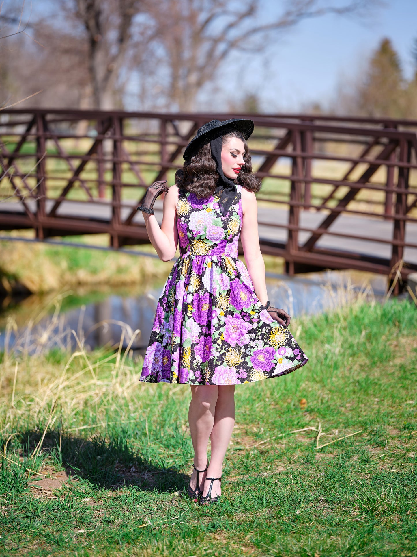 a model standing in front of a bridge wearing the purple metallic floral vintage dress