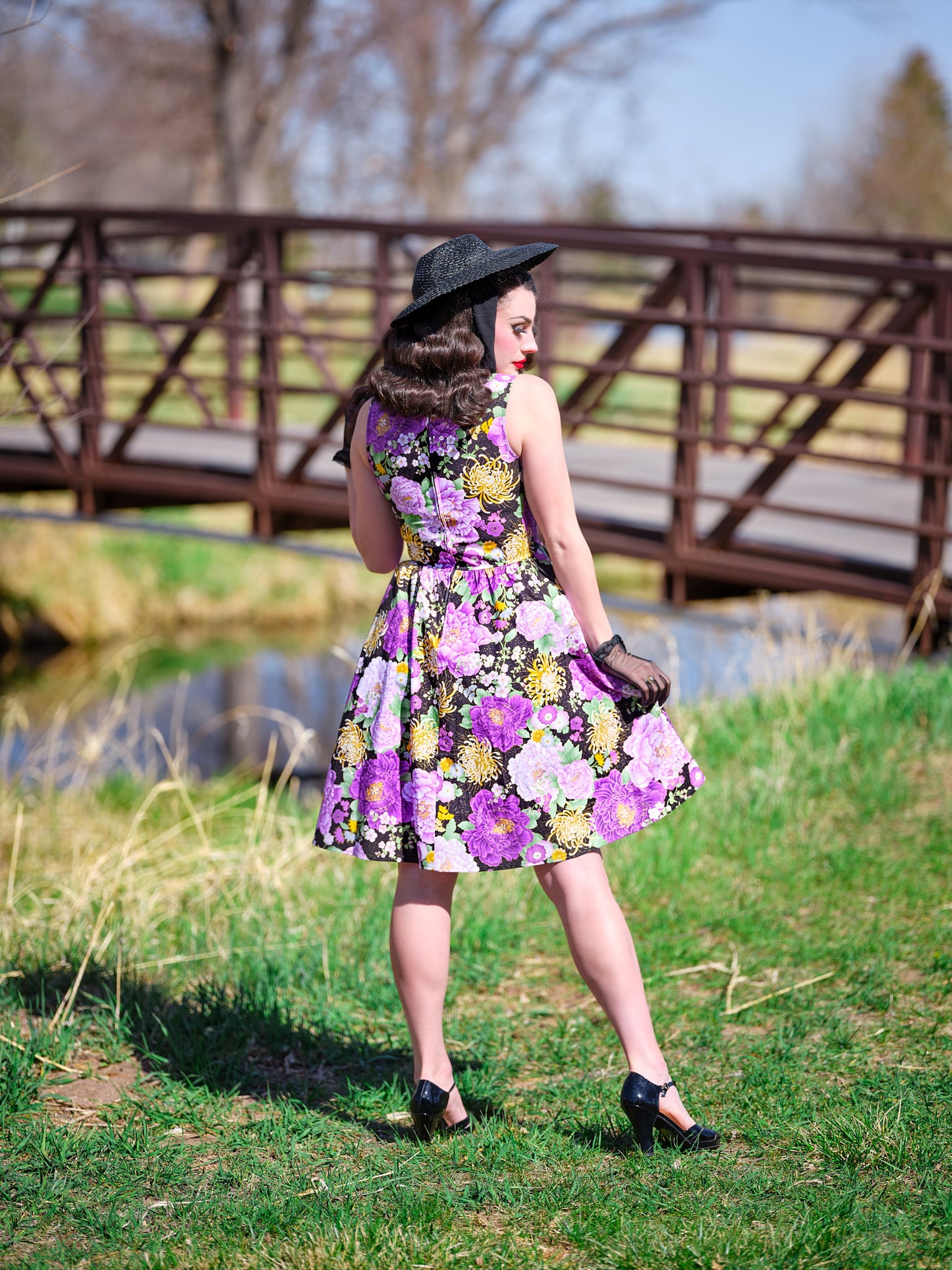 a back of a model standing in front of a bridge wearing the purple metallic floral vintage dress