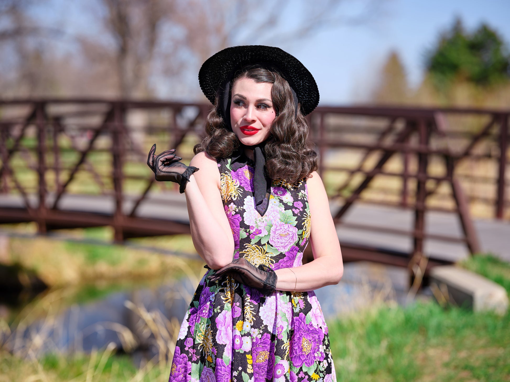 a close up of a model standing in front of a bridge wearing the purple metallic floral vintage dress