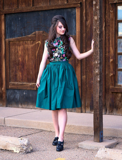 a full size image of model standing in front of a wooden wall and wearing the peggy swing skirt in green