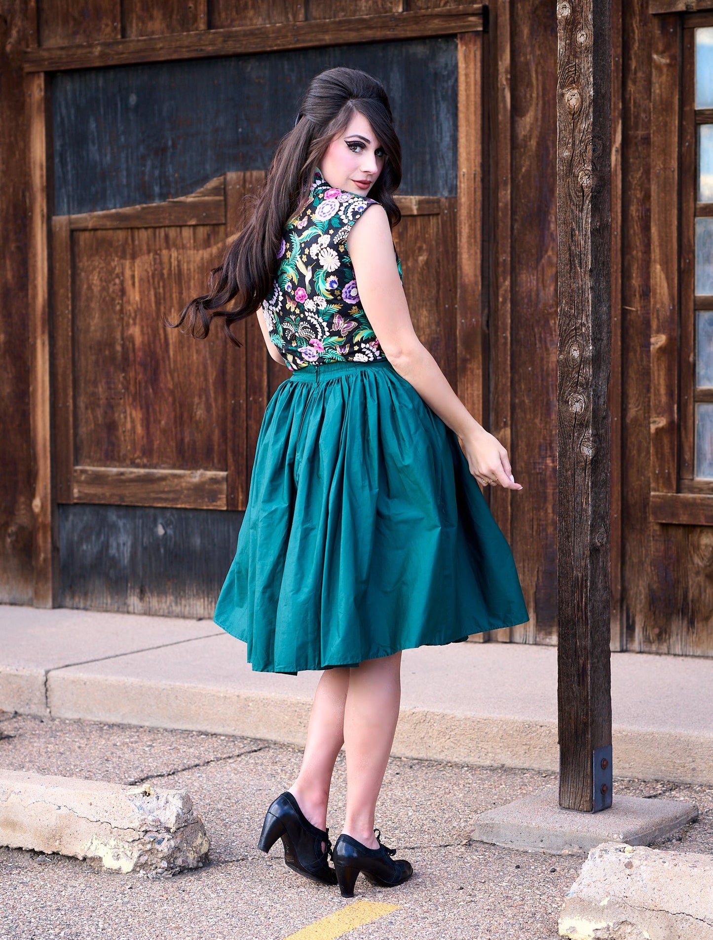 a full size image of a back side of a model standing in front of a wooden wall and wearing the peggy swing skirt in green