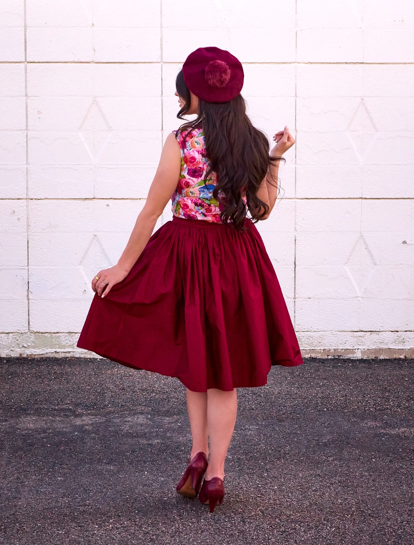 a full size image of a back side of a model standing in front of a white wall wearing the watercolor floral bow top