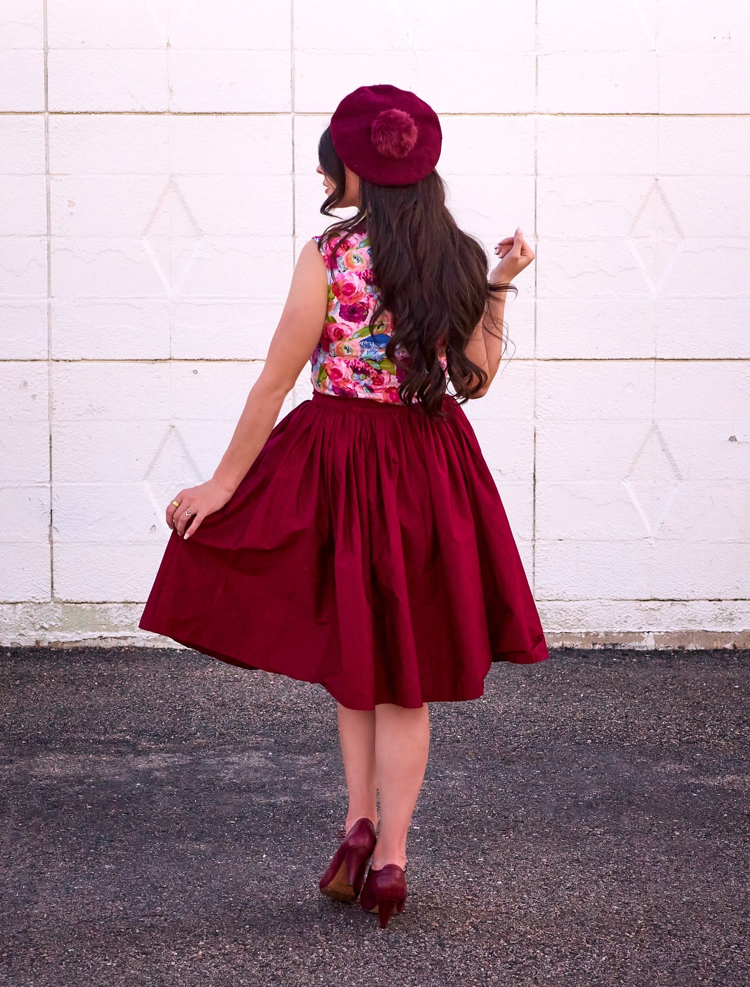 a full size image of the back side of a model standing in front of a white wall wearing the peggy swing skirt in burgundy