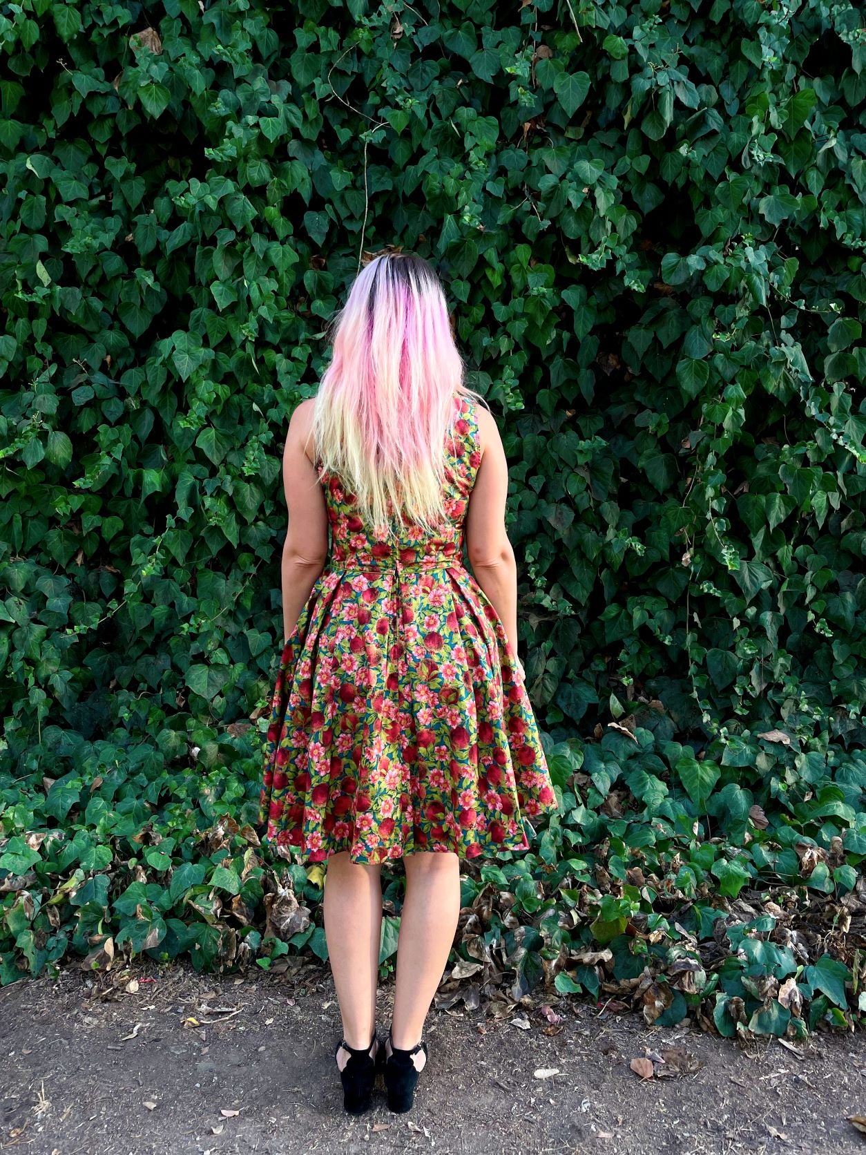a full length image of a back of a model standing in front of leafy backdrop wearing the Elizabeth dress in pomegranate 